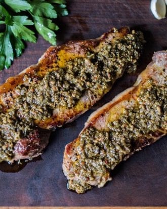 Title: "Chimichurri-Infused Grilled Delicacy" Alternative Text: Two succulent grilled meat strips generously coated with vibrant chimichurri sauce, placed on a dark wooden background accompanied by fresh parsley leaves.