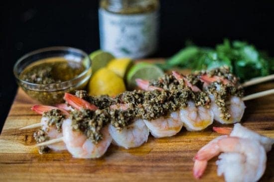 Tender shrimp skewers, generously coated with J&M's rich Chimichurri, paired with fresh citrus on a rustic wooden board. A feast for both eyes and palate.